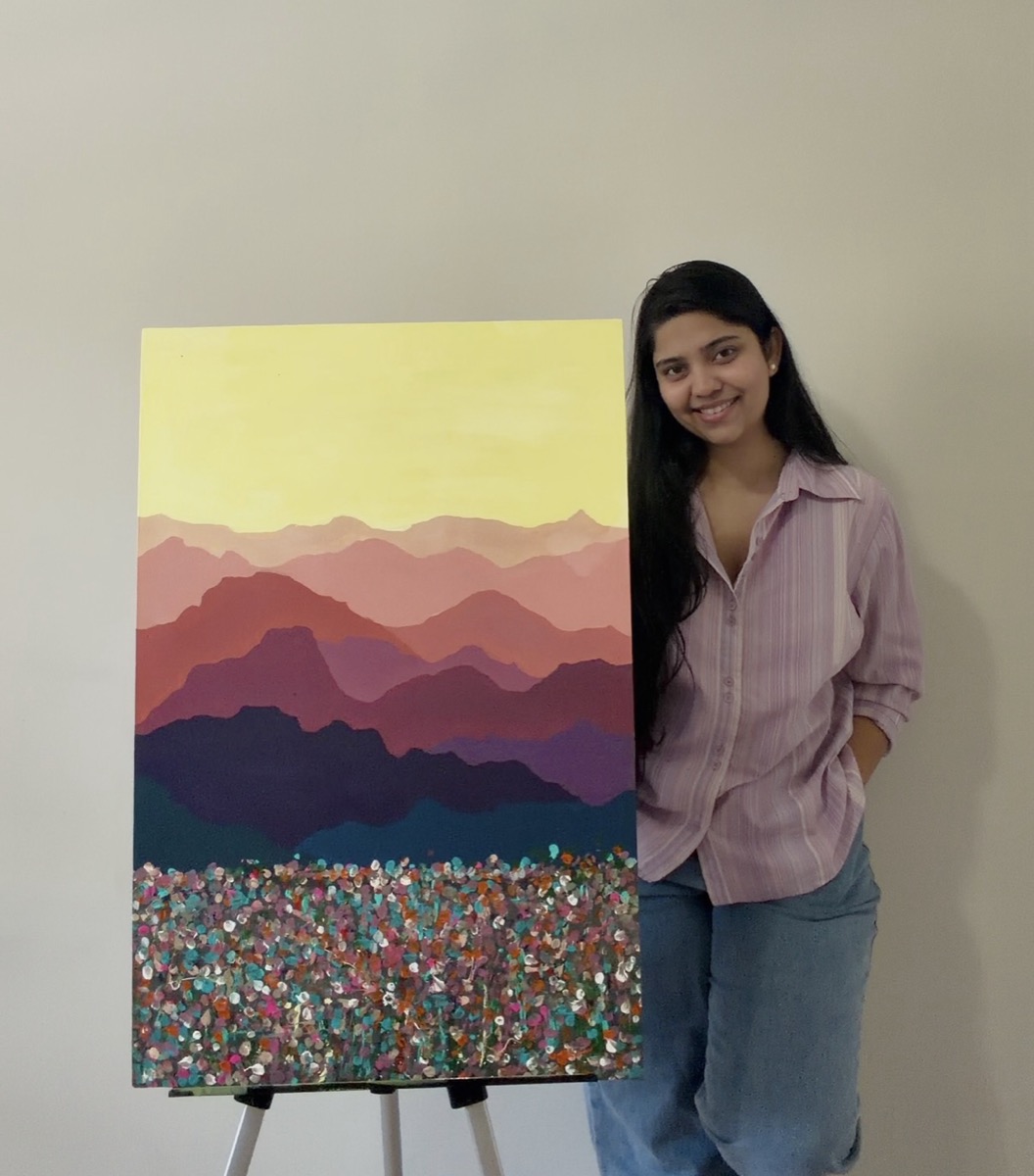 Aashna standing beside one of her paintings on an easel